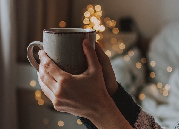 Hands holding warm drink, fairy lights, cosy home. Ways to ease anxiety naturally.